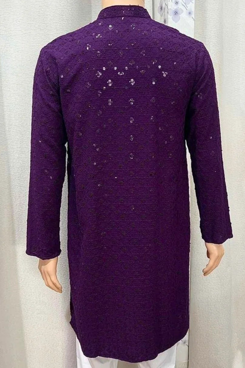 Person wearing a purple kurta with white pants standing in front of white curtains.
